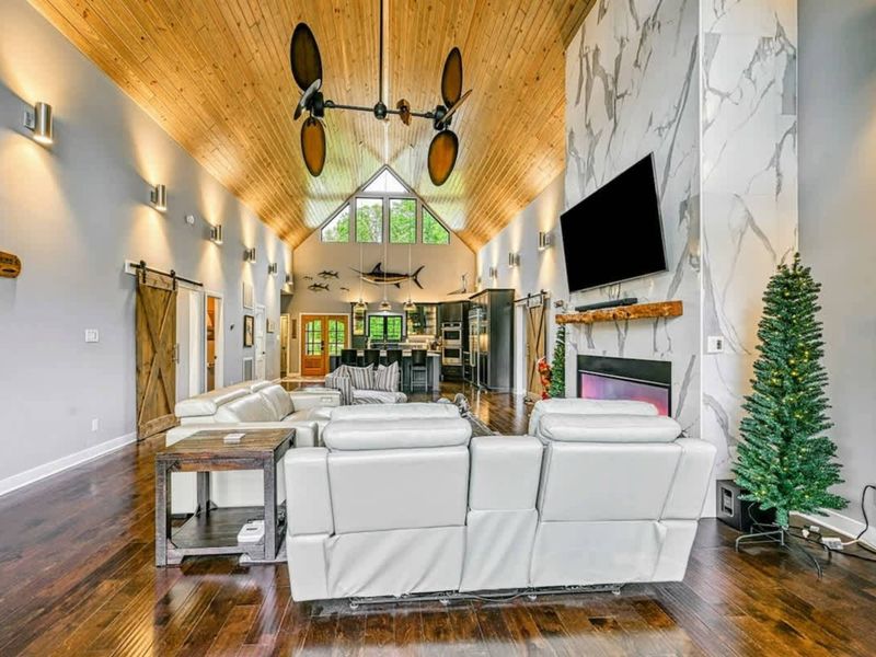 Great Room Reverse - Looking from the kitchen back through the full great room toward the marble fireplace, barn doors, and A-frame glass peak.