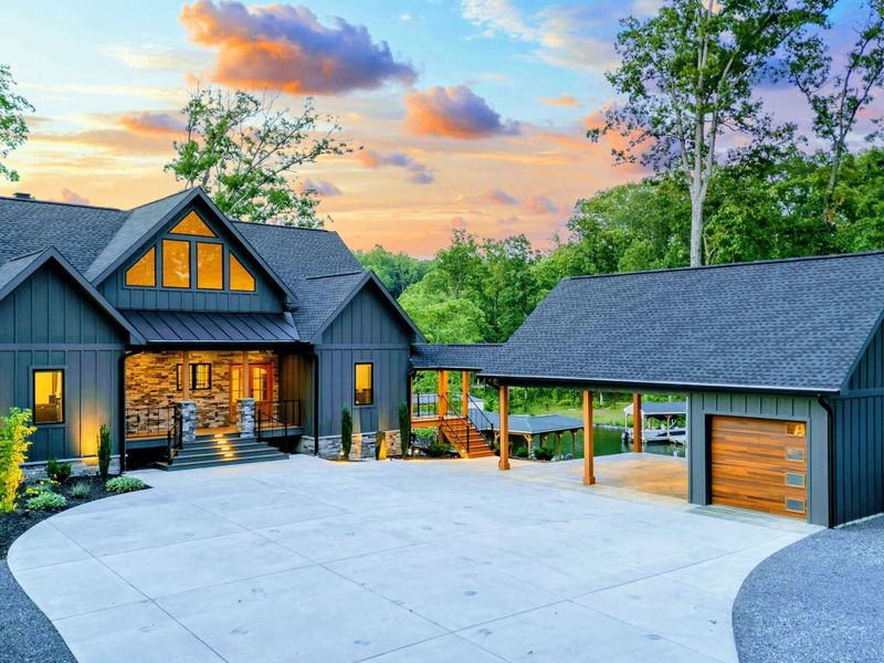 Twilight Aerial - Another angle at sunset showing the home, garage, driveway, and covered side porch with the lake visible beyond.
