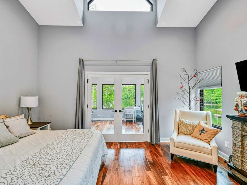Upper Primary Suite - The king bedroom features French doors to the screened porch, a stone fireplace, accent chair, and treetop views through the windows.