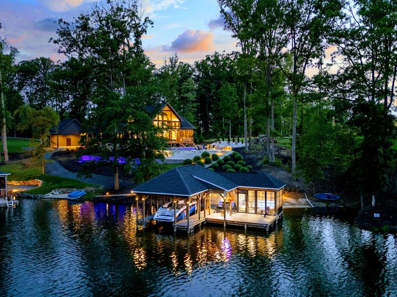 Twilight Aerial - A breathtaking aerial at sunset reveals the lit home, boathouse with bar, glowing pool, and the surrounding lake and cove.