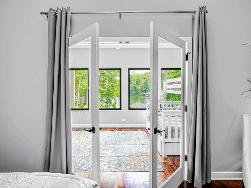 Upper Primary View - French doors open to the screened sunroom, where a white rocking chair and crib sit surrounded by windows overlooking the lake.