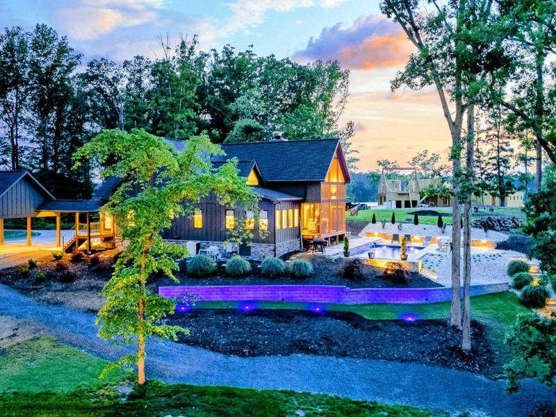 Twilight Grounds - The home, pool, and grounds glow with warm uplighting and purple pool LEDs as sunset colors fill the sky.