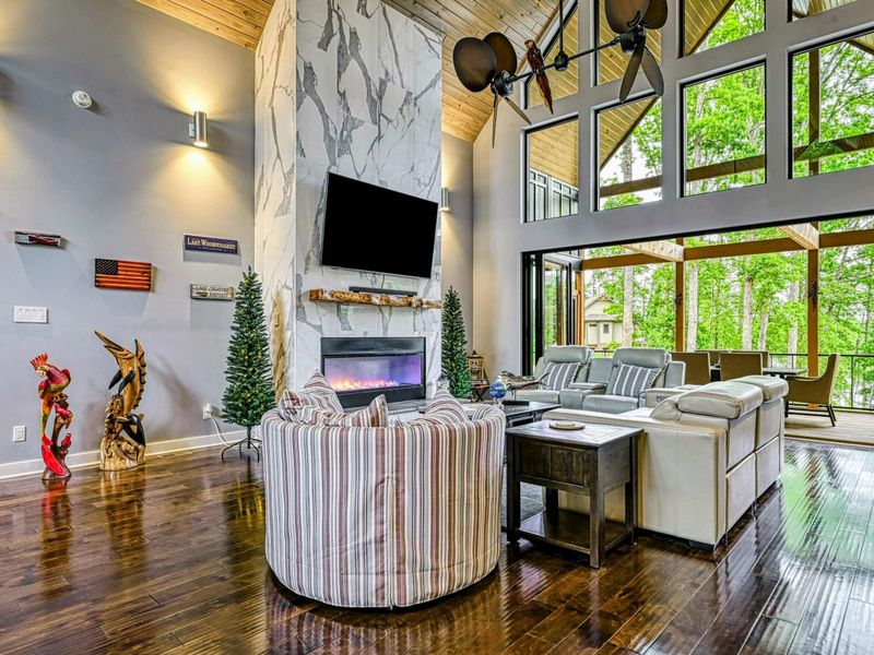 Great Room - The full two-story space with marble fireplace, mounted TV, dual ceiling fans, rustic barn doors, and striped accent chairs on gleaming hardwood floors.