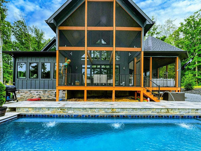 Pool and Home - The dark-sided modern craftsman with its dramatic A-frame glass wall rises behind the pool, screened porch, and stone patio.