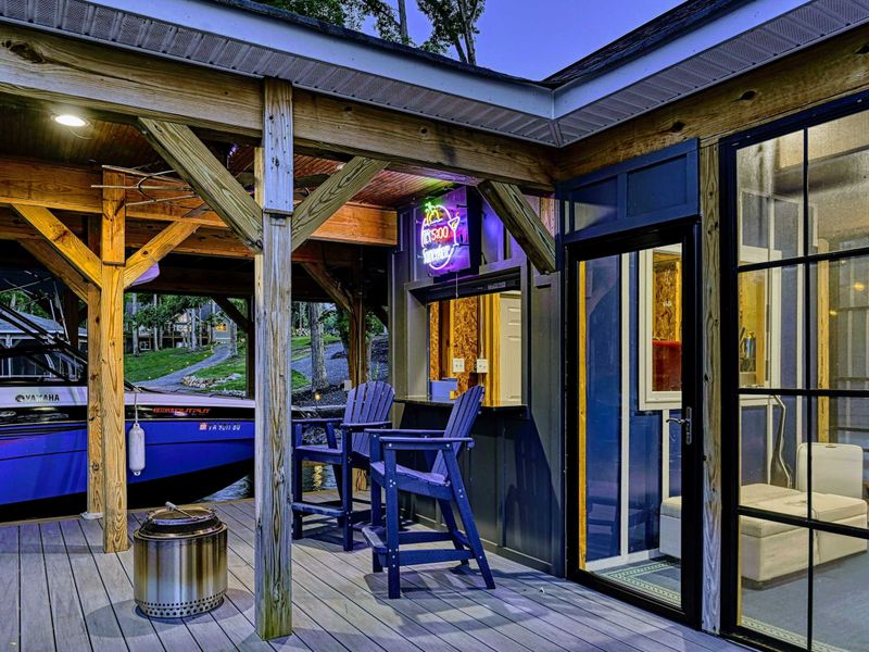 Dock at Twilight - The full boathouse and bar area glows at dusk, with the screened lounge, boat slip, and surrounding trees reflected in the water.