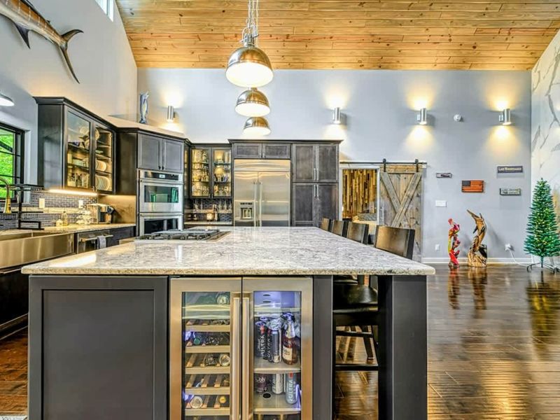 Kitchen Island - The granite island features a built-in wine cooler and beverage fridge, with dark cabinetry and professional-grade appliances beyond.