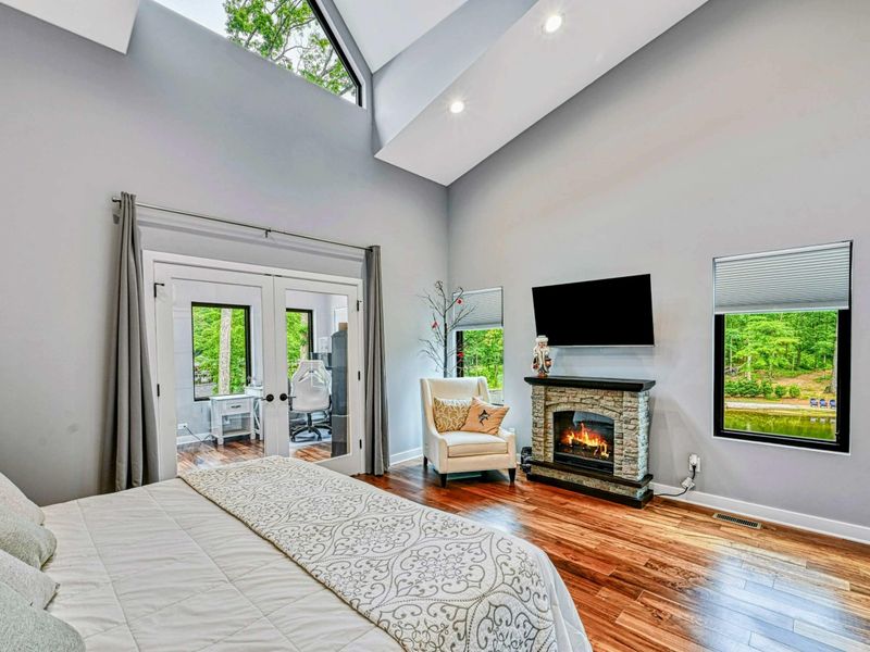 Upper Primary Suite - A king bed with skylights, vaulted ceilings, a stone electric fireplace, Smart TV, and French doors opening to the screened porch with lake views.