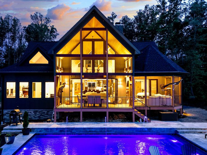 Twilight Aerial - A stunning aerial view at dusk shows the illuminated home, glowing pool, dock, and reflections on the lake's still water.