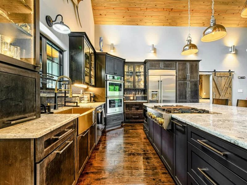 Kitchen Counter - A closer view of the granite countertops, copper farmhouse sink, and dark glass-front cabinetry beneath industrial pendant lights.