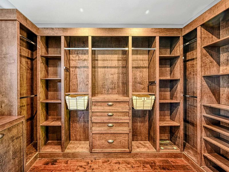 Walk-in Closet - A custom-built walk-in closet in rich warm wood with shelving, drawers, and hanging space connects to the primary bathroom.