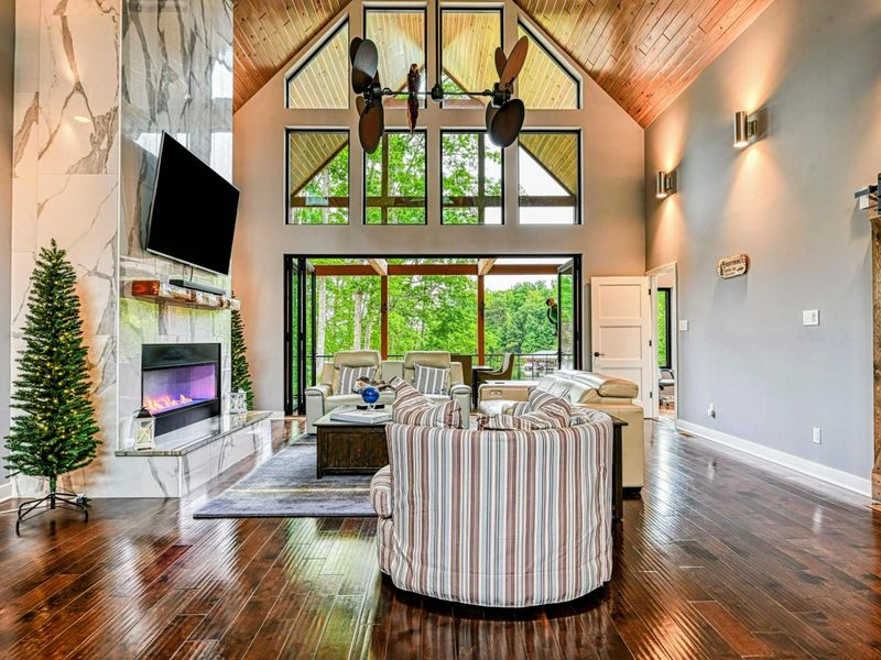 Great Room - Soaring pine-clad cathedral ceilings, a floor-to-ceiling marble electric fireplace, leather seating, and marlin wall art define this dramatic open-concept living space.