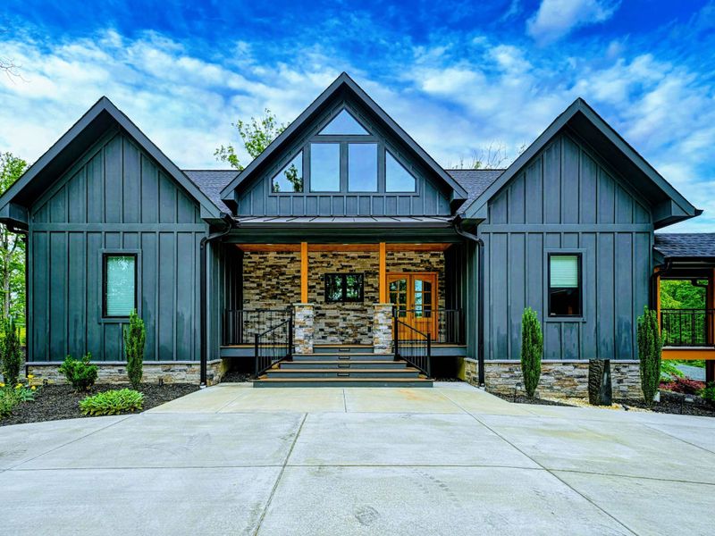 Front Exterior - The modern craftsman facade features dark board-and-batten siding, stacked stone entry columns, timber accents, and a covered porch.