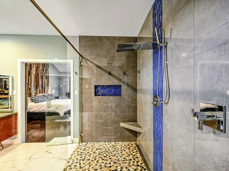 Primary Shower - Another angle showing the shower's pebble floor, multiple shower heads, and glass enclosure with a view back to the bedroom.