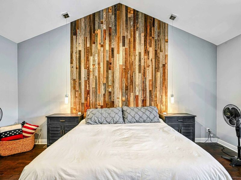 Primary Suite Headboard - The reclaimed wood plank accent wall with pendant bedside lighting creates a warm, rustic focal point in the primary bedroom.