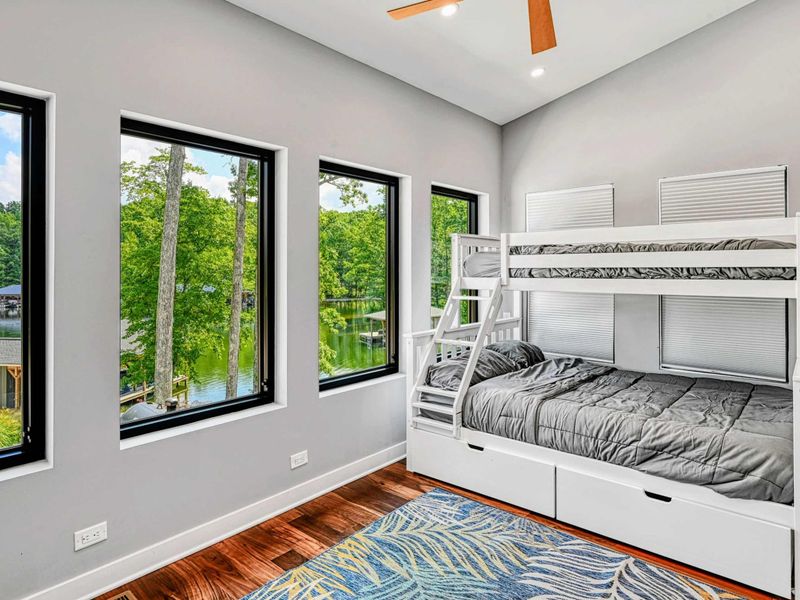 Bunk Room - A white twin-over-full bunk bed with built-in storage drawers sits in front of windows overlooking the lake and dock through the trees.
