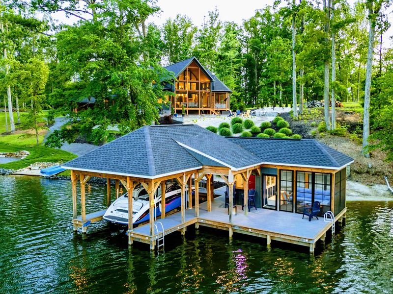 Aerial Dock View - From above, the covered boathouse with its dual-room layout, dock platform, and boat slip are on full display beside the wooded shoreline.