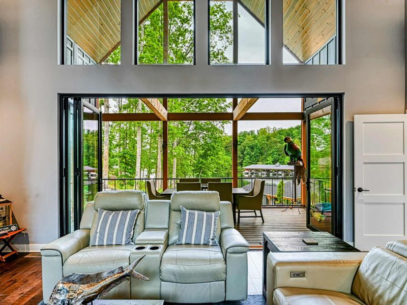 Great Room - Leather recliners face the screened porch through floor-to-ceiling glass doors, with the double-height A-frame ceiling and natural light beyond.