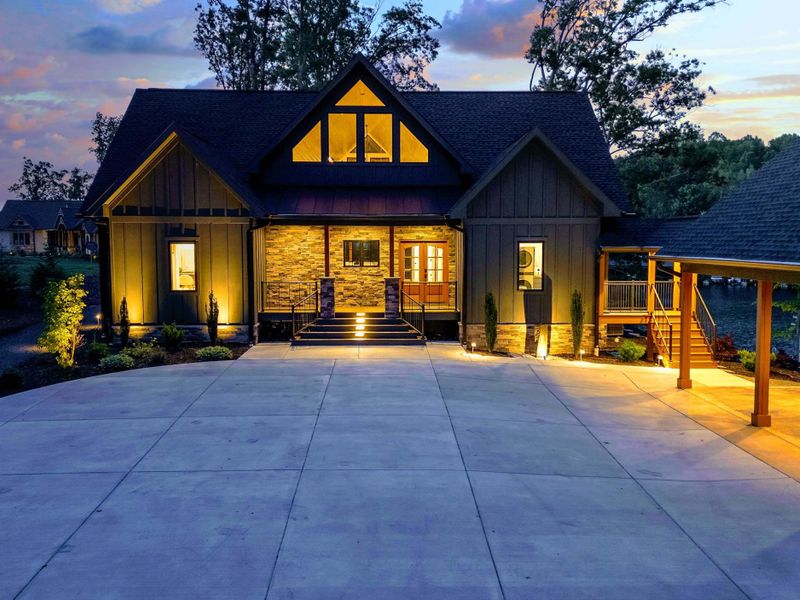 Twilight Entry - The full front elevation at dusk, with stone columns, warm interior glow, and a sweeping concrete driveway.