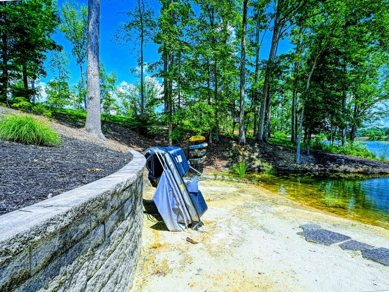 Beach Access - A stone retaining wall path leads down to the natural shoreline and shallow water entry, with kayaks stored nearby.