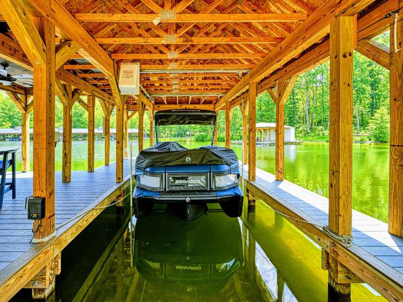 Boat Slip - The covered timber-framed boat slip houses a wakeboard boat on the lift, with dock seating and ceiling fan overhead.