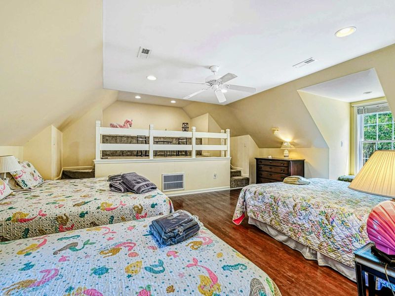 Upper Level Bunk Room - Multiple queen and twin beds with colorful quilts, loft railing, ceiling fan, and hardwood floors.