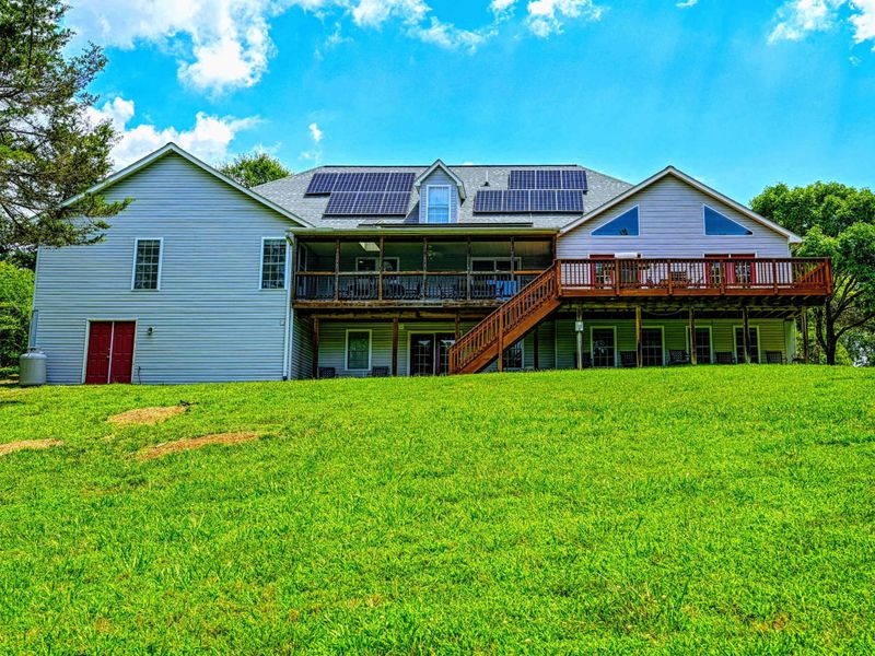 Exterior - Lakeside view showing the large deck, screened porch, and solar panels across the roofline.