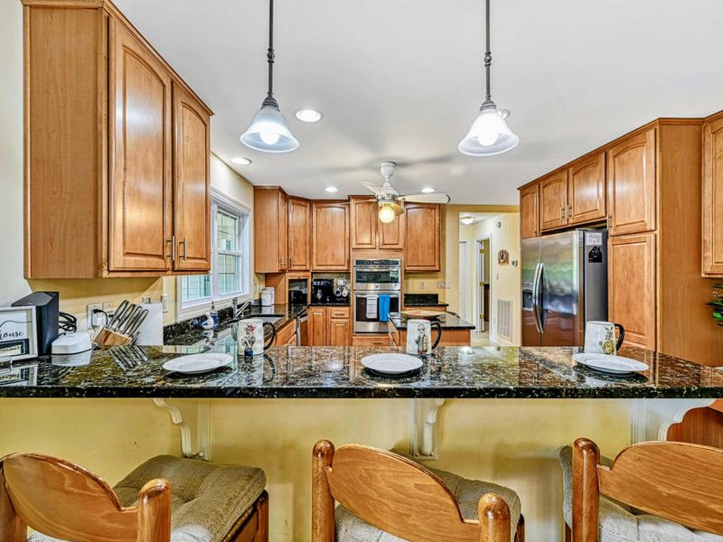 Kitchen - Breakfast bar with four stools, pendant lights, and granite countertops ready for casual meals.