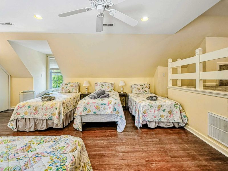 Upper Level Twin Room - Three twin beds side by side with sea creature quilts, loft railing, and ceiling fan.