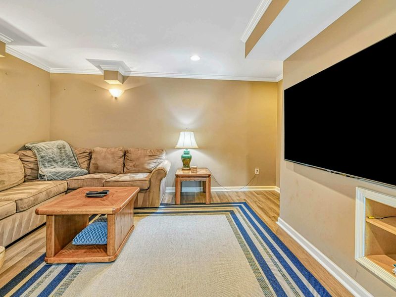Lower Level Media Room - Large wall-mounted TV with sectional seating, teal accent lamps, and cozy lounge setting.
