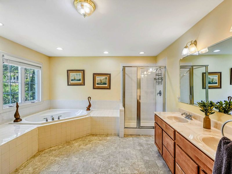 Primary Bathroom - Corner soaking tub, glass-door walk-in shower, wood double vanity, and nautical ship paintings.