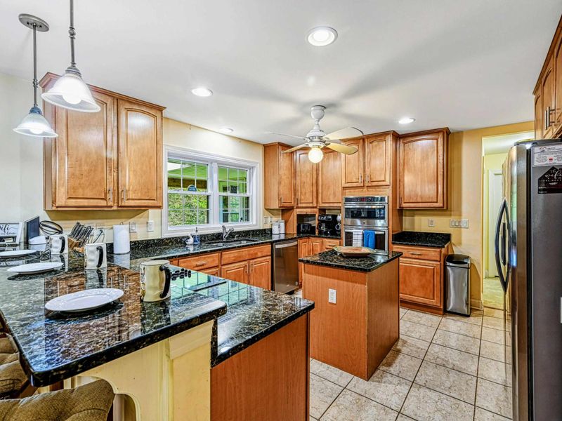 Kitchen - Pendant lights over the breakfast bar with maple cabinets, wall ovens, and stainless refrigerator.