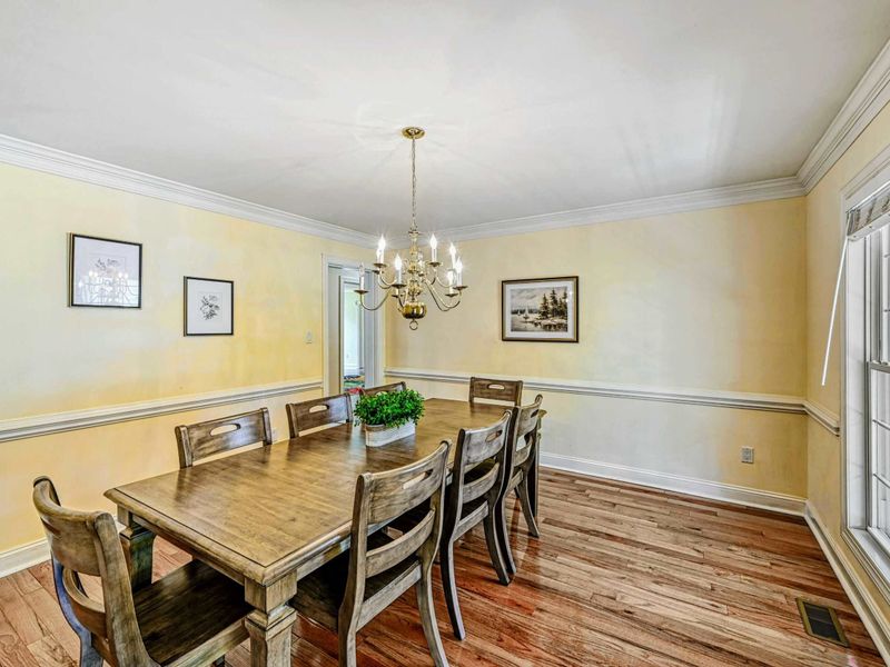 Formal Dining Room - Wood table for eight beneath a brass chandelier with crown molding and hardwood floors.