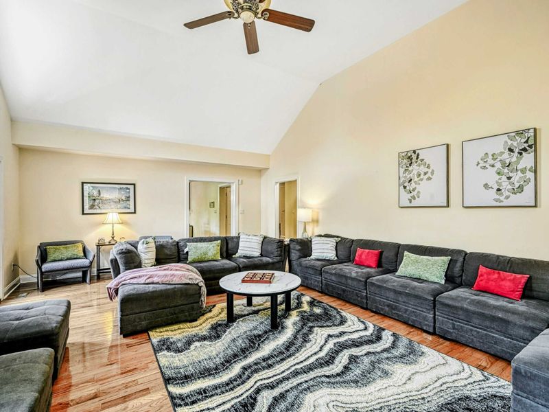 Living Room - Alternate angle of the vaulted great room with sectional, wave-pattern rug, and botanical wall art.
