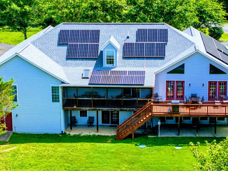 Aerial - Close view of the rear showing solar panels, wraparound deck, screened porch, and summer canopy.