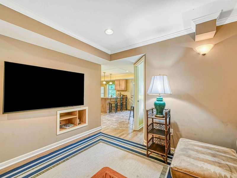 Lower Level Media Room - TV wall with passageway to the lower kitchenette and rattan accent lamp.