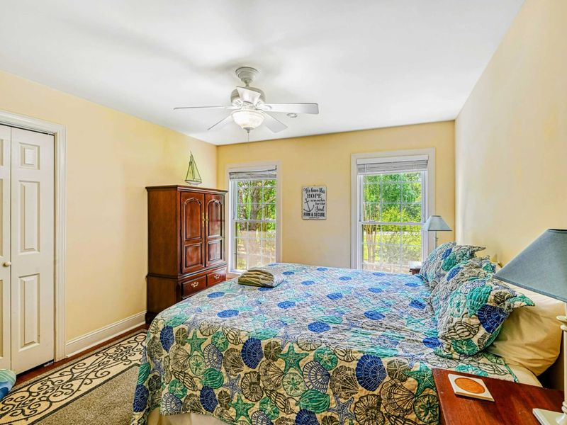 Bedroom 2 - King bed with coastal shell-print bedding, cherry armoire, ceiling fan, and garden-view windows.