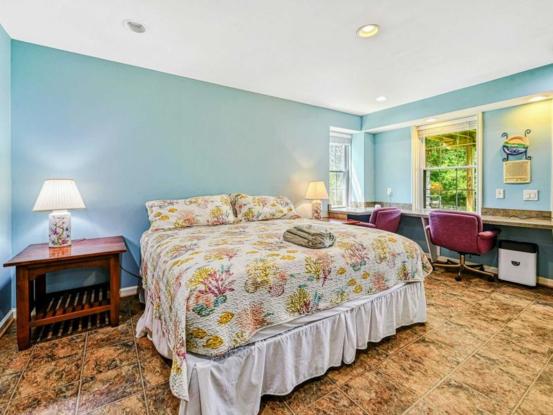 Bedroom 5 - King bed with coral reef quilt in sky blue walls, desk area with chairs, and tile floors on the lower level.