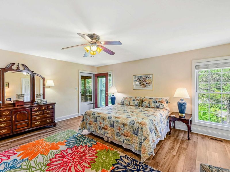 Primary Suite - Alternate angle showing the dresser with tri-fold mirror, glass door, and colorful floral rug.