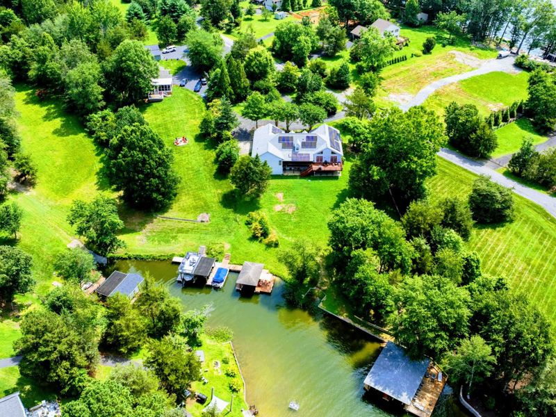 Aerial - Full property view with the sweeping lawn, covered dock, fire pit, and lake frontage.