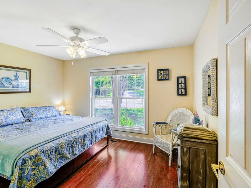 Bedroom 4 - King bed with tropical palm bedding on cherry hardwood floors with beach art and wicker accent chair.