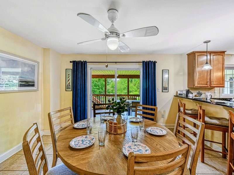 Dining Area - Round oak table set for six with ceiling fan, blue curtains, and sliding door to the screened porch.