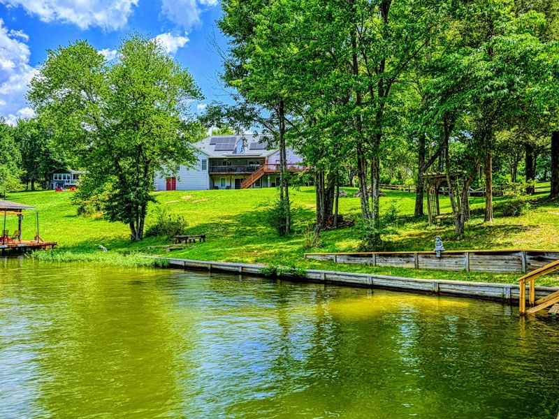 Waterfront - View from the dock looking up the sloping green lawn toward the home through mature trees.