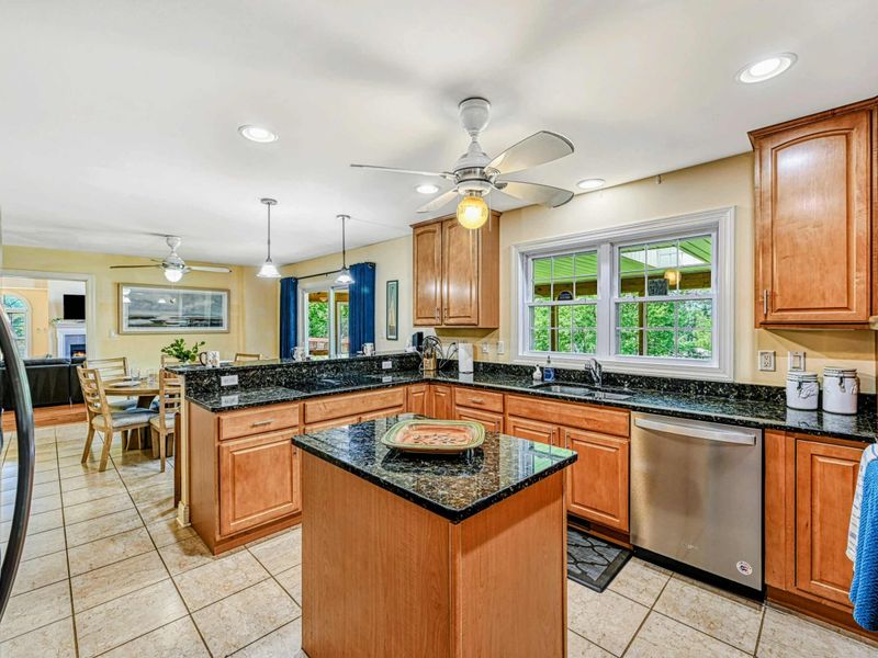 Kitchen - Maple cabinets with dark granite countertops, center island, ceiling fan, and open sightline to the dining area.