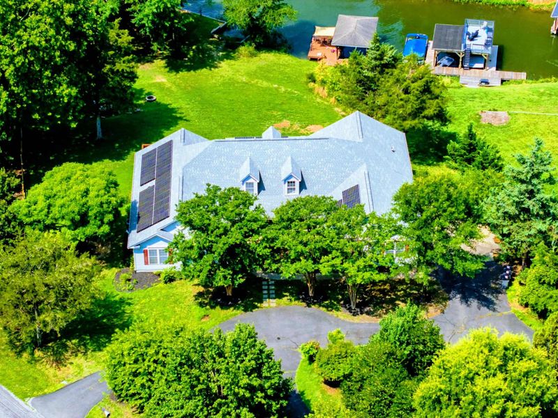 Aerial - Front of the home from above showing dormer windows, solar panels, circular driveway, and mature trees.