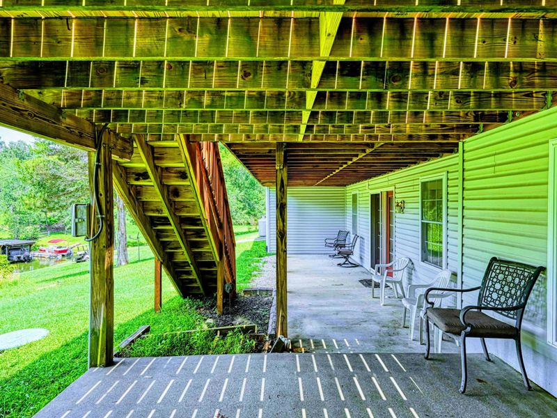 Lower Patio - Covered area beneath the upper deck with seating, concrete pad, and stairway to the yard.