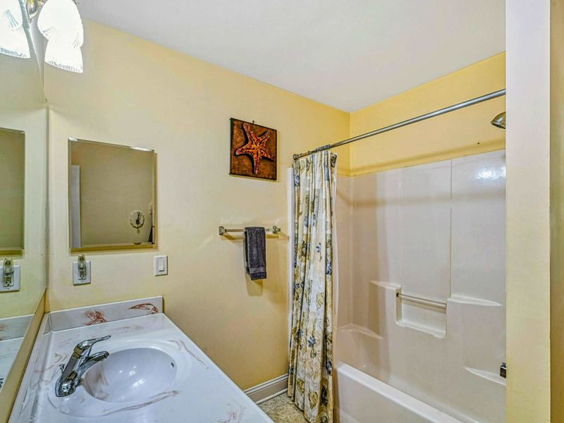 Bathroom - Single vanity with starfish art and tub/shower combo with a floral curtain.