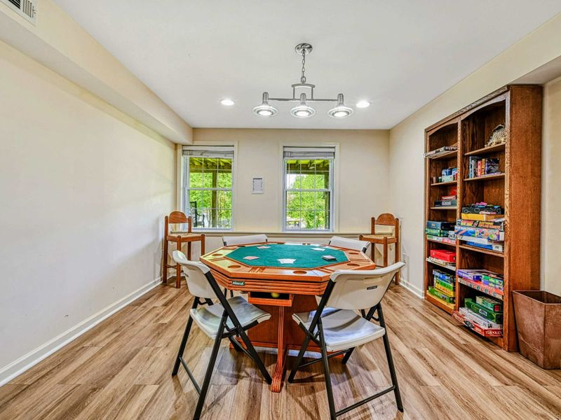 Game Room - Poker table with green felt top, folding chairs, and a bookshelf filled with board games and puzzles.