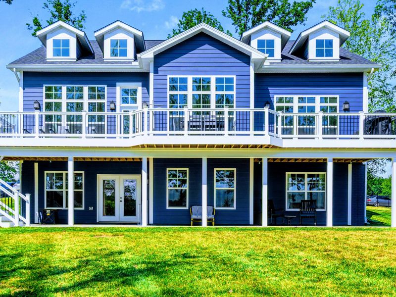 Rear Facade - White railings, dormer windows, and a covered lower porch wrap the back of the home with outdoor living space.