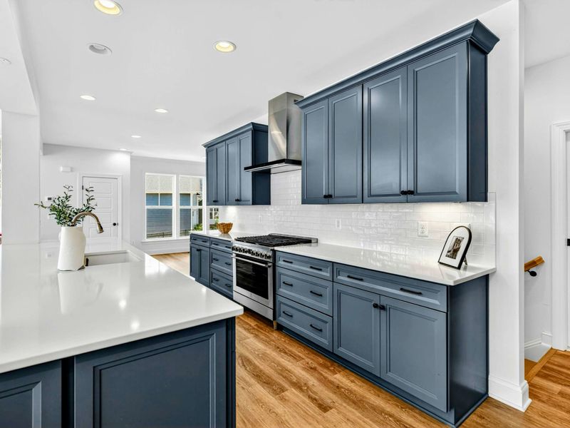 Kitchen View - A wide angle showing the gas range, blue cabinetry, and a sightline straight to the lake through the dining room windows.
