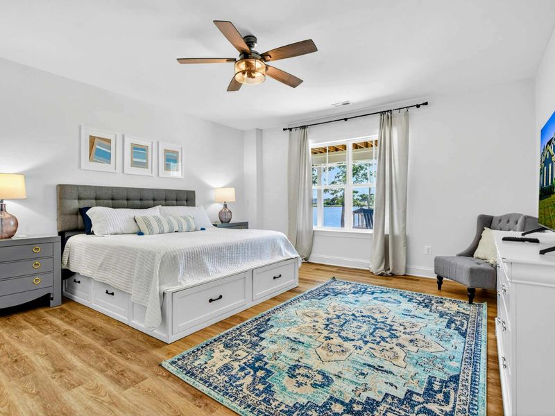 Main Level Bedroom - A king bed with under-bed storage, gray tufted headboard, Smart TV, and lake-view windows.